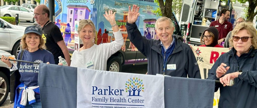 Parker volunteers waving behind a Parker banner at an outdoor event