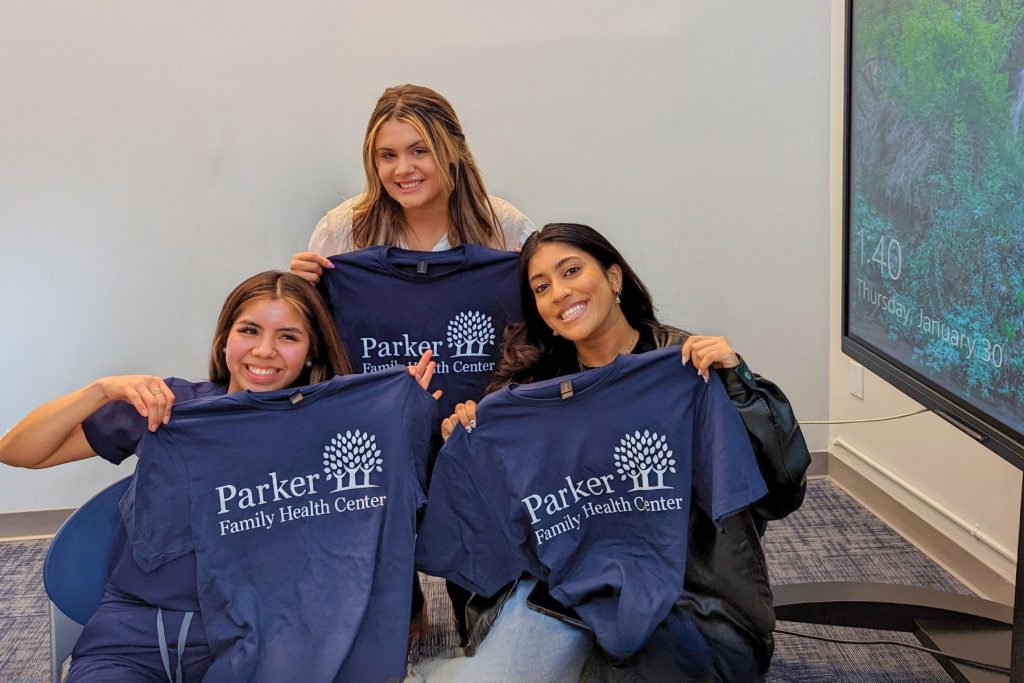 Three volunteers holding up navy Parker Family Health Center T-shirts